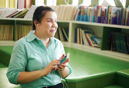 Una chica invidente interactúa con su móvil escuchando el lector de voz con unos cascos enchufados al dispositivo móvil.
