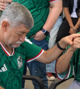 El aficionado, vestido con la camiseta de México y colocando sus manos sobre las del intérprete.